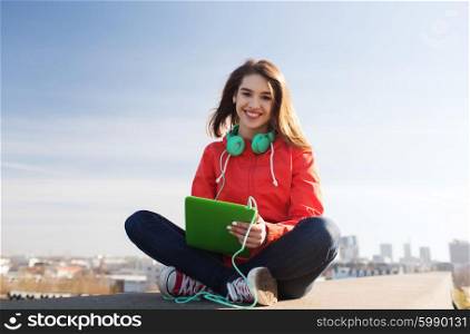 technology, lifestyle, music and people concept - smiling young woman or teenage girl with tablet pc computer and headphones outdoors