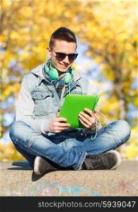 technology, lifestyle, season, music and people concept - smiling young man or teenage boy with tablet pc computer and headphones over autumn park background