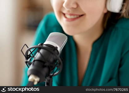 technology, mass media and people concept - close up of woman with microphone and headphones talking and recording podcast at studio. woman with microphone recording podcast at studio