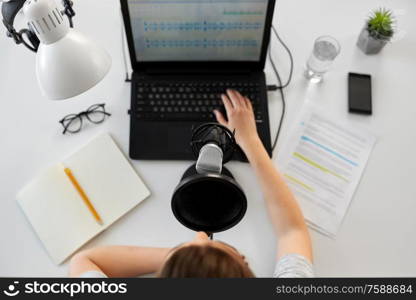 technology, mass media and people concept - woman with microphone and laptop computer reading text from papers and recording podcast at studio. woman with microphone recording podcast at studio