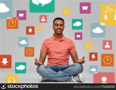 technology, media and people concept - happy indian mant meditating in lotus yoga pose over app icons on grey background. happy man in yoga lotus pose over app icons