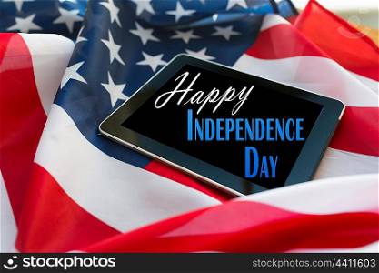 technology, memorial day, patriotism and nationalism concept - happy independence day words on tablet pc computer screen on american flag