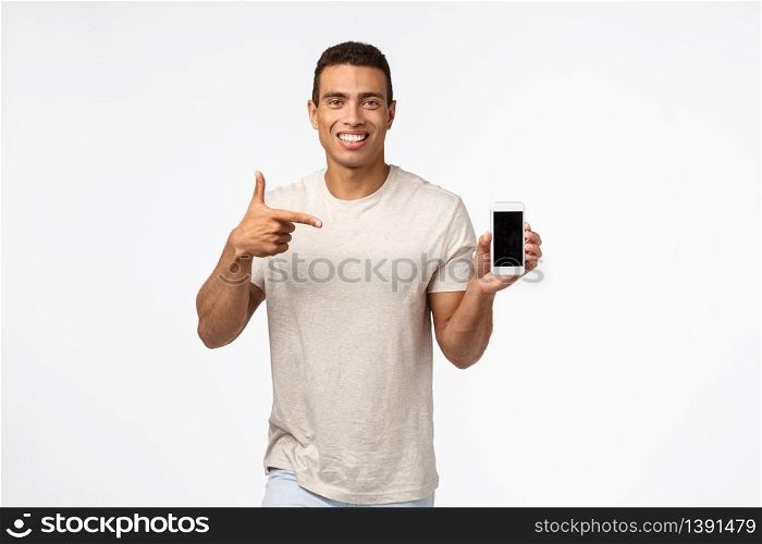 Technology, mobile gadget and people concept. Cheerful good-looking brazilian athletic man recommend fitness app, looking at calories or diet advices, holding smartphone, pointing mobile, smiling.. Technology, mobile gadget and people concept. Cheerful good-looking brazilian athletic man recommend fitness app, looking at calories or diet advices, holding smartphone, pointing mobile, smiling