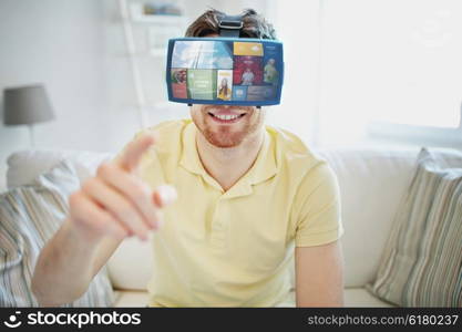 technology, multimedia, mass media, entertainment and people concept - happy young man in virtual reality headset or 3d glasses with media or web applications at home