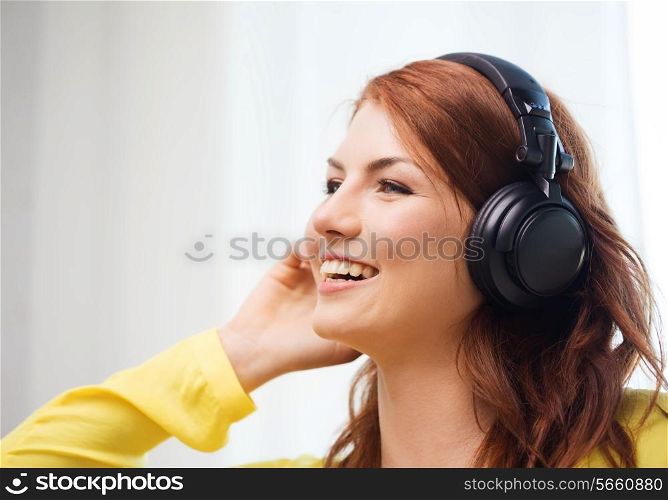 technology, music and happiness concept - smiling teenage girl in headphones at home