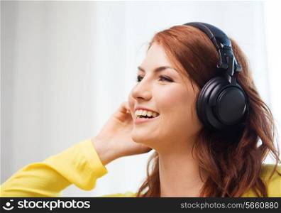 technology, music and happiness concept - smiling teenage girl in headphones at home