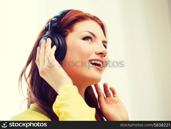 technology, music and happiness concept - smiling teenage girl in headphones at home