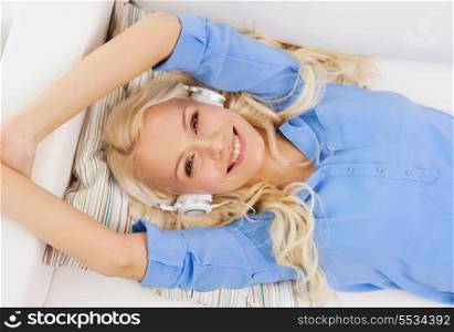 technology, music and happiness concept - smiling young girl lying on sofa in headphones at home