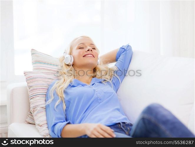technology, music and happiness concept - smiling young girl lying on sofa in headphones at home