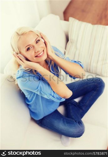 technology, music and happiness concept - smiling young girl sitting on sofa in headphones at home