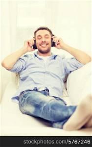 technology, music and happiness concept - smiling young man in headphones at home