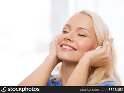 technology, music and happiness concept - smiling young woman in headphones at home