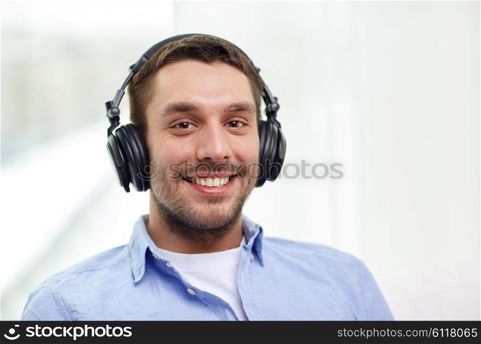 technology, music and people concept - smiling young man in headphones at home