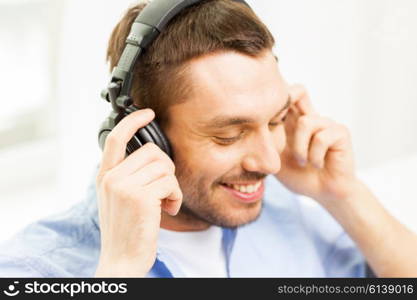 technology, music and people concept - smiling young man in headphones at home