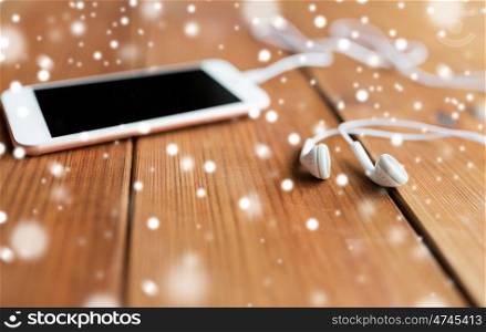 technology, music, gadget and object concept - close up of white smartphone and earphones on wooden surface with copy space
