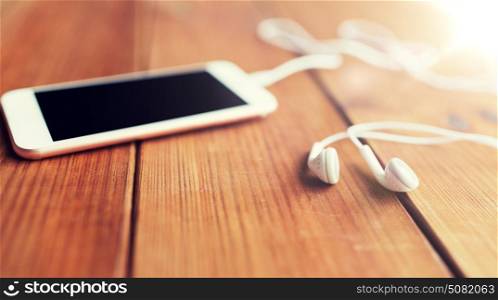 technology, music, gadget and object concept - close up of white smartphone and earphones on wooden surface with copy space. close up of blank smartphone and earphones on wood