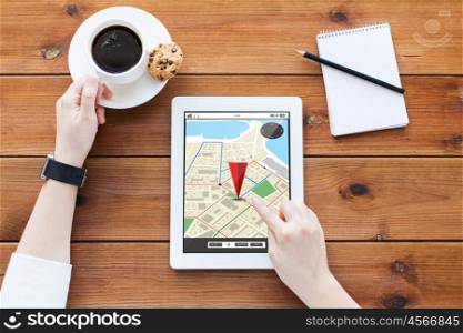 technology, navigation, location and people concept - close up of woman with gps navigator map on tablet pc computer screen, notebook and coffee on wooden table