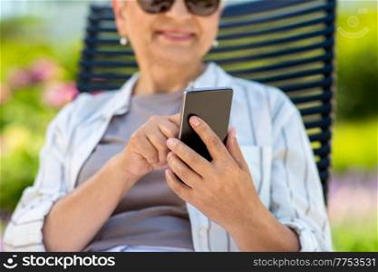 technology, old age and people concept - close up of happy smiling senior woman with smartphone resting at summer garden. close up of woman with phone at summer garden