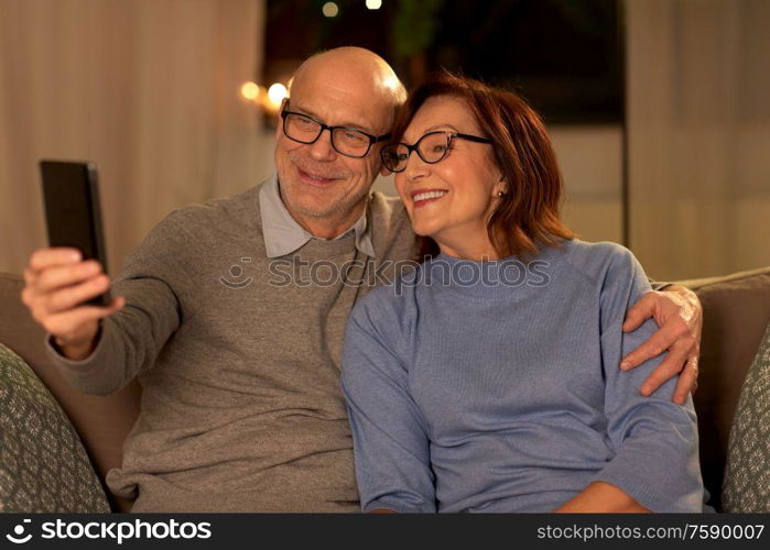 technology, old age and people concept - happy senior couple taking selfie with smartphone at home in evening. old couple taking selfie with smartphone at home