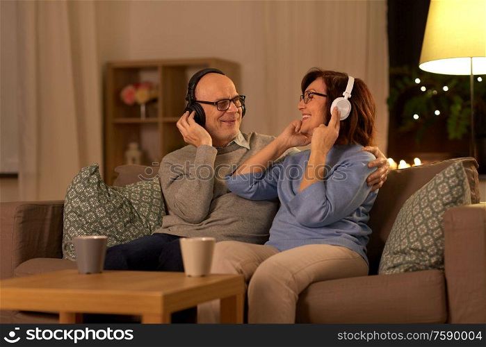 technology, old age and people concept - happy senior couple with headphones listening to music at home in evening. senior couple with headphones listening to music