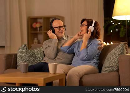 technology, old age and people concept - happy senior couple with headphones listening to music at home in evening. senior couple with headphones listening to music