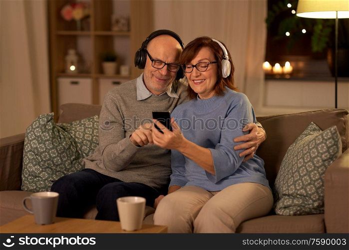 technology, old age and people concept - happy senior couple with smartphone and headphones at home in evening. senior couple with smartphone and headphones