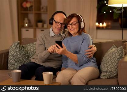 technology, old age and people concept - happy senior couple with smartphone and headphones at home in evening. senior couple with smartphone and headphones