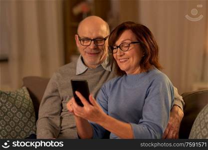 technology, old age and people concept - happy senior couple with smartphone at home in evening. happy senior couple with smartphone at home