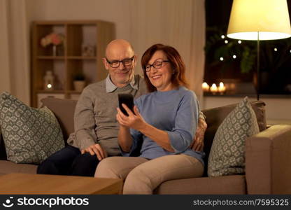 technology, old age and people concept - happy senior couple with smartphone at home in evening. happy senior couple with smartphone at home