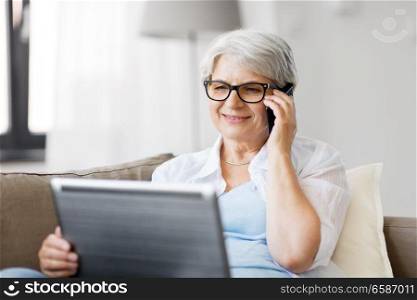 technology, old age and people concept - happy senior woman in glasses with laptop computer calling on smartphone at home. senior woman with laptop calling on smartphone