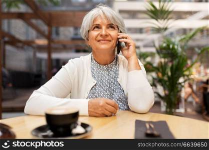 technology, old age and people concept - happy senior woman with coffee calling on smartphone at street cafe. senior woman calling on smartphone at street cafe