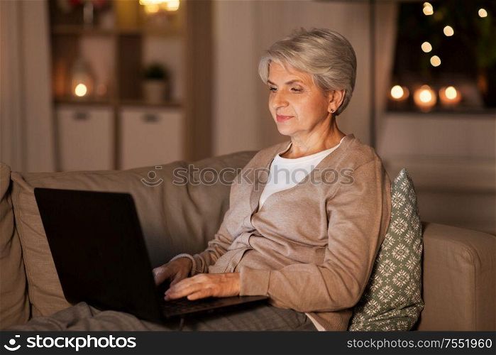 technology, old age and people concept - happy senior woman with laptop computer at home in evening. happy senior woman with laptop at home at night