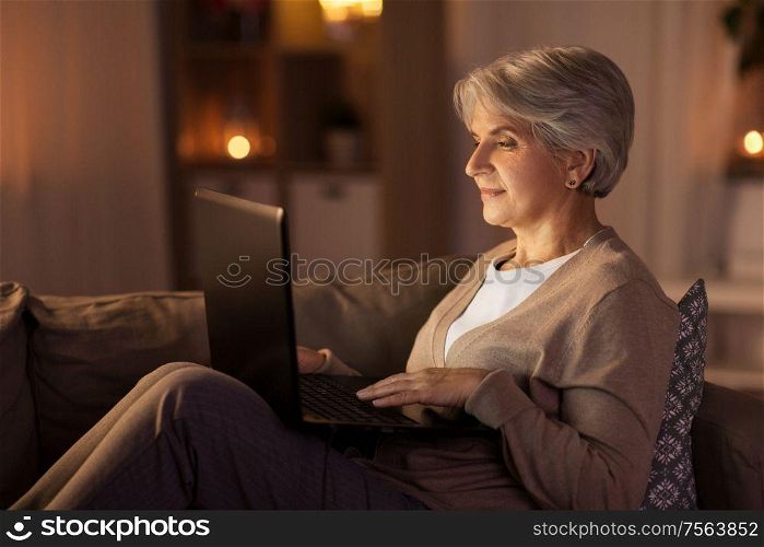 technology, old age and people concept - happy senior woman with laptop computer at home in evening. happy senior woman with laptop at home at night
