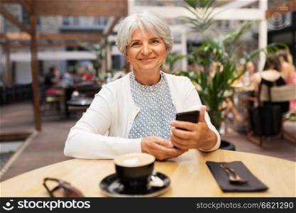 technology, old age and people concept - happy senior woman with smartphone at street cafe. happy senior woman with smartphone at street cafe