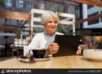 technology, old age and people concept - happy senior woman with tablet pc and coffee at street cafe. senior woman with tablet pc and coffee at cafe