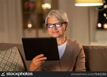 technology, old age and people concept - happy senior woman with tablet pc computer at home in evening. happy senior woman with tablet pc at home at night