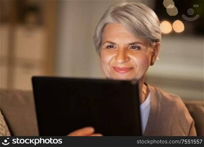 technology, old age and people concept - happy senior woman with tablet pc computer at home in evening. happy senior woman with tablet pc at home at night