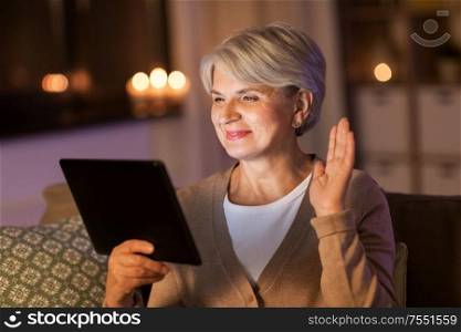 technology, old age and people concept - happy senior woman with tablet pc computer having video chat at home in evening. happy senior woman with tablet pc at home at night