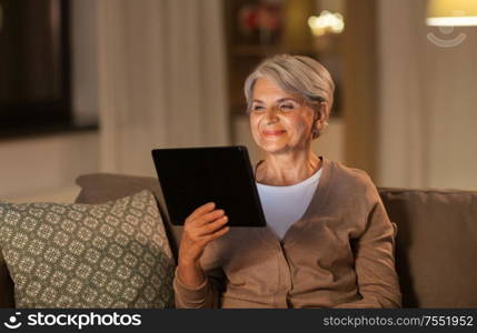 technology, old age and people concept - happy senior woman with tablet pc computer at home in evening. happy senior woman with tablet pc at home at night