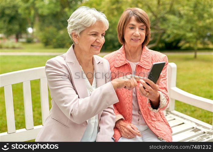 technology, old age and people concept - happy senior women or female friends with smartphone at summer park. happy senior women with smartphone at summer park
