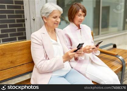 technology, old age and people concept - happy senior women or friends with smartphones sitting on bench in city. happy senior women with smartphones in city