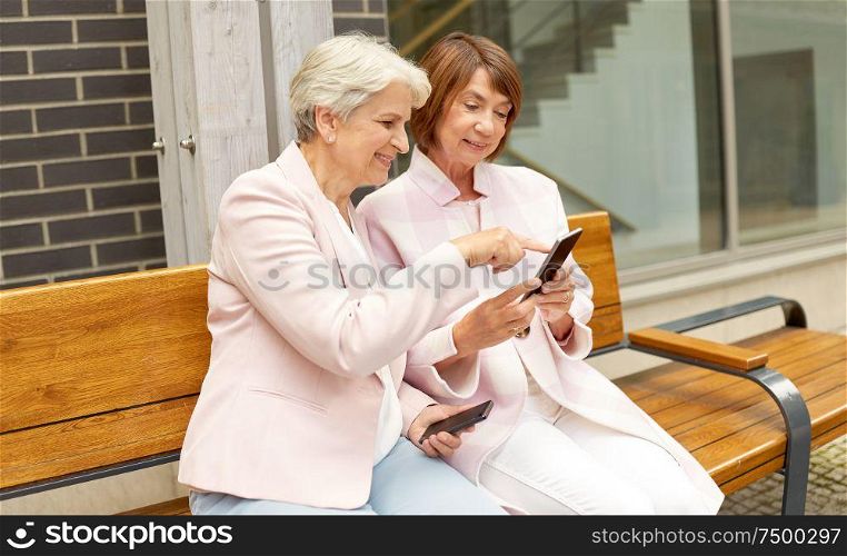 technology, old age and people concept - happy senior women or friends with smartphones sitting on bench in city. happy senior women with smartphones in city