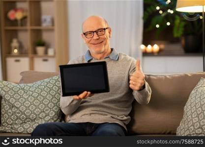 technology, old age and people concept - happy smiling bald senior man with tablet pc computer sitting on sofa and showing thumbs up at home in evening. happy senior man with tablet computer at home