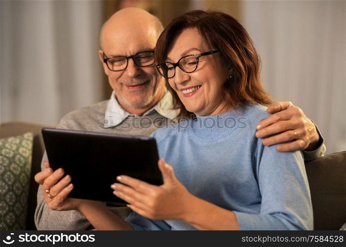 technology, old age and people concept - happy smiling senior couple with tablet pc computer at home in evening. happy senior couple with tablet pc at home