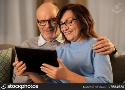 technology, old age and people concept - happy smiling senior couple with tablet pc computer at home in evening. happy senior couple with tablet pc at home