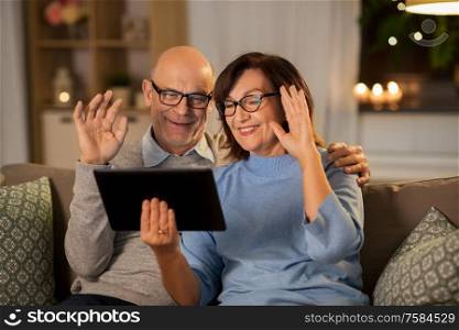 technology, old age and people concept - happy smiling senior couple with tablet pc computer having video call at home in evening. old couple with tablet pc has video call at home