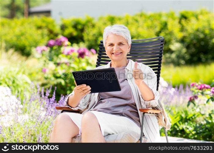 technology, old age and people concept - happy smiling senior woman with tablet pc computer resting at summer garden and showing thumbs up. happy senior woman with tablet pc at summer garden