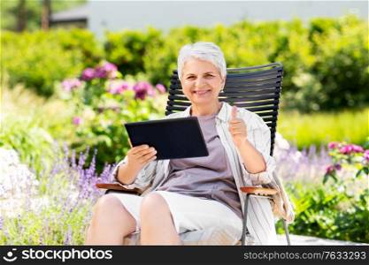 technology, old age and people concept - happy smiling senior woman with tablet pc computer resting at summer garden and showing thumbs up. happy senior woman with tablet pc at summer garden