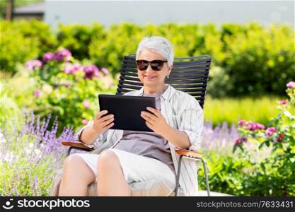 technology, old age and people concept - happy smiling senior woman with tablet pc computer resting at summer garden. happy senior woman with tablet pc at summer garden