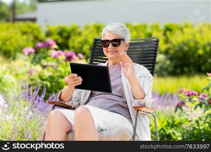 technology, old age and people concept - happy smiling senior woman with tablet pc computer having video call and waving hand at summer garden. happy senior woman with tablet pc at summer garden